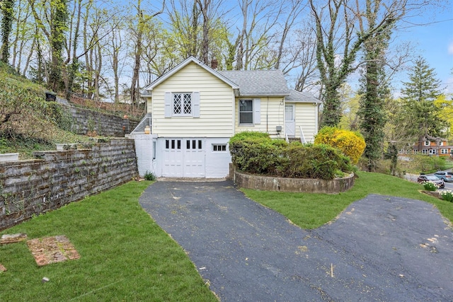 traditional-style house featuring a front lawn, driveway, roof with shingles, and a garage