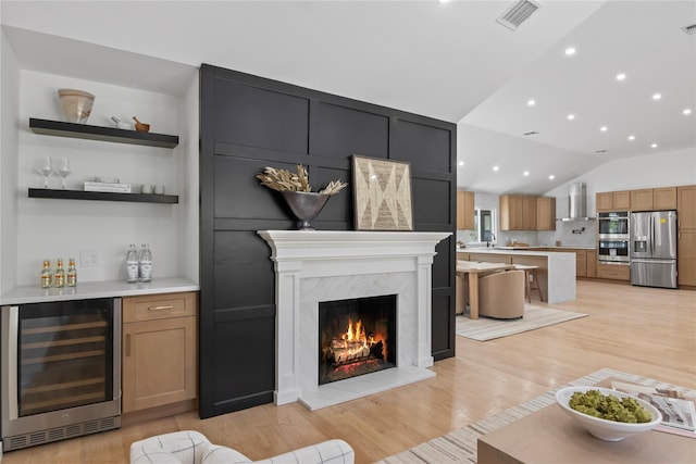 living room featuring visible vents, vaulted ceiling, a bar, beverage cooler, and light wood-style floors