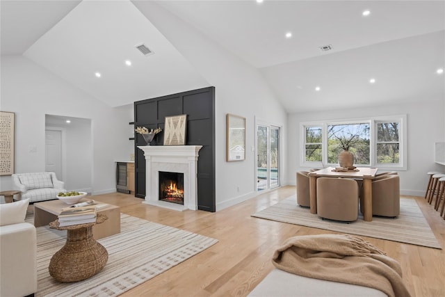 living area with a lit fireplace, high vaulted ceiling, and visible vents