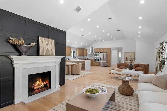 living room featuring light wood-style floors, visible vents, lofted ceiling, and a high end fireplace