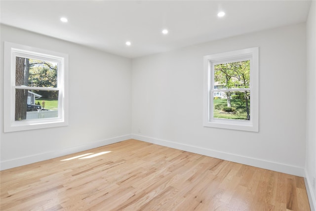 spare room featuring baseboards, a healthy amount of sunlight, and light wood finished floors