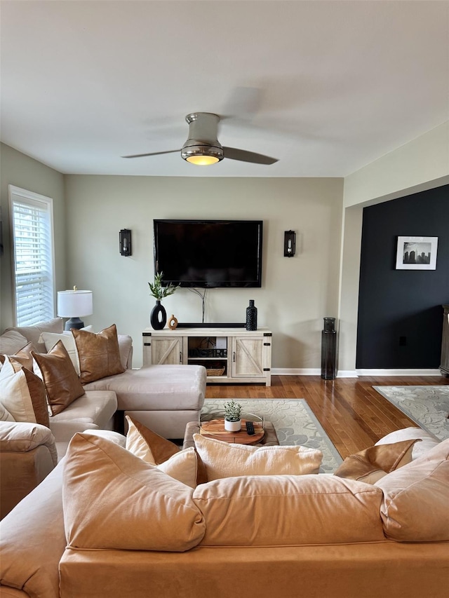 living area with baseboards, wood finished floors, and ceiling fan