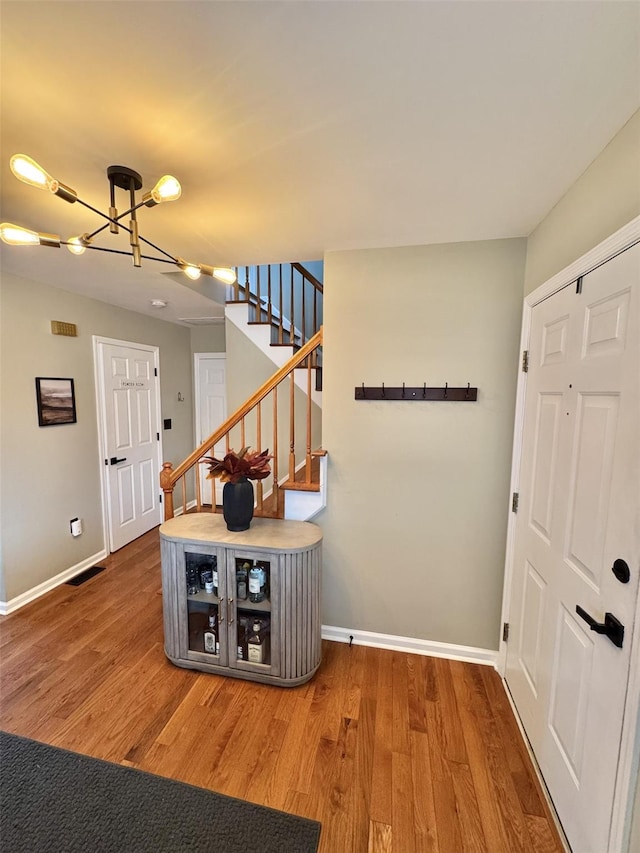 entrance foyer with stairway, wood finished floors, visible vents, baseboards, and a chandelier