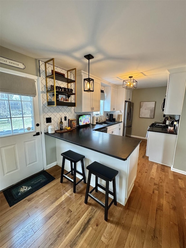 kitchen with stainless steel fridge with ice dispenser, dark countertops, a sink, a peninsula, and white cabinetry