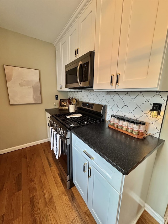kitchen featuring white cabinets, dark wood-style flooring, baseboards, backsplash, and appliances with stainless steel finishes