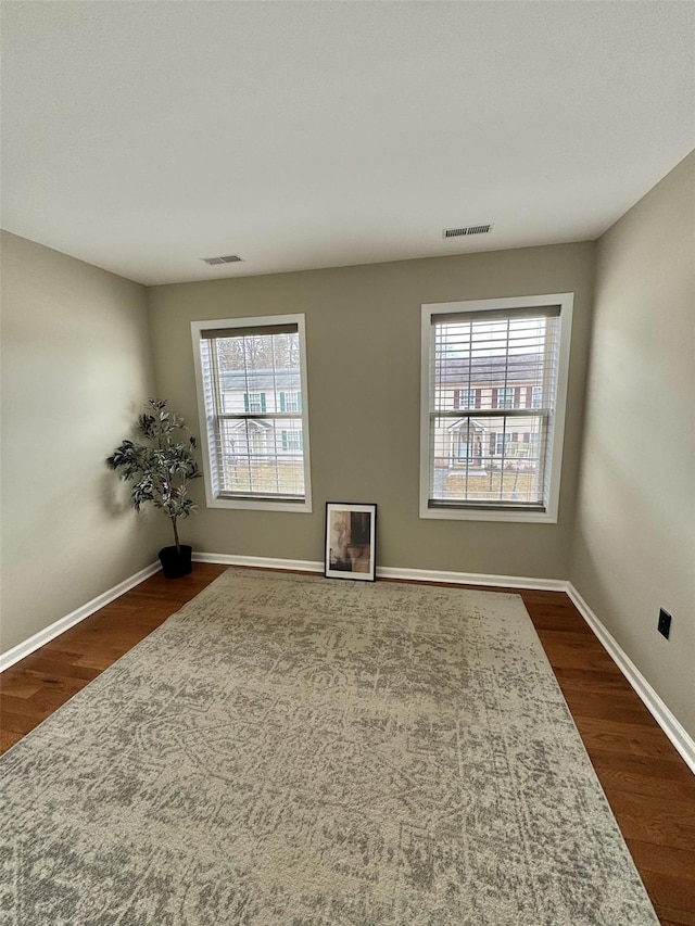 empty room with visible vents, baseboards, and dark wood-style flooring