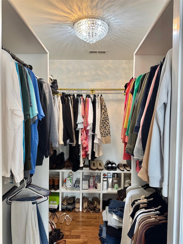 spacious closet with wood finished floors, visible vents, and a chandelier