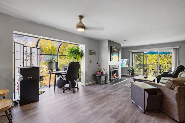 living area featuring wood finished floors, a ceiling fan, a lit fireplace, and baseboards