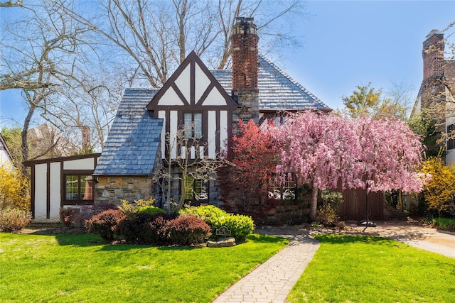 view of front of house with stone siding, a front lawn, a chimney, and a high end roof