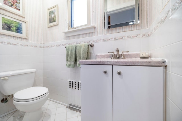 half bathroom with radiator, tile patterned floors, toilet, vanity, and tile walls