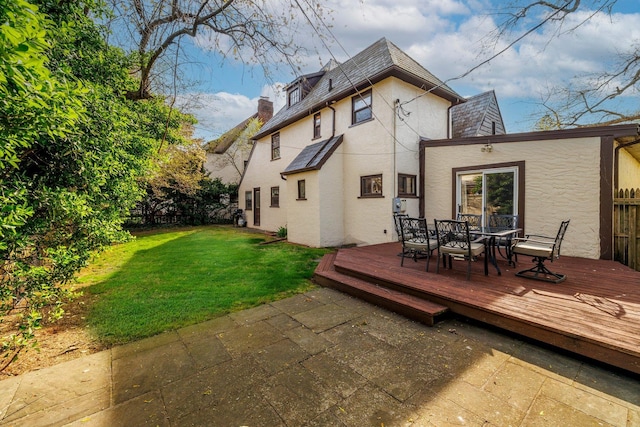 back of property with fence, a lawn, a deck, outdoor dining area, and stucco siding