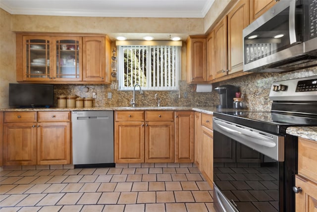 kitchen with a sink, tasteful backsplash, crown molding, light stone counters, and appliances with stainless steel finishes