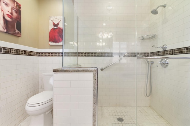 bathroom with toilet, a stall shower, tile walls, and wainscoting