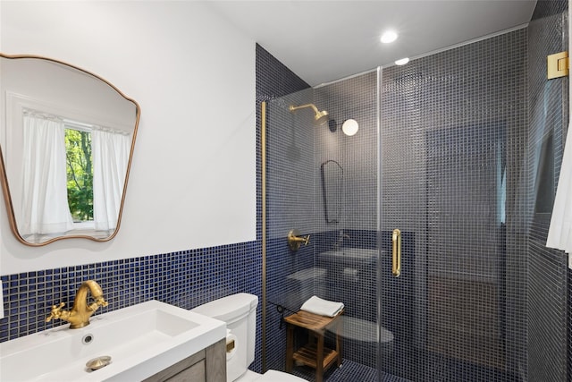 full bath featuring tile walls, wainscoting, a shower stall, vanity, and toilet