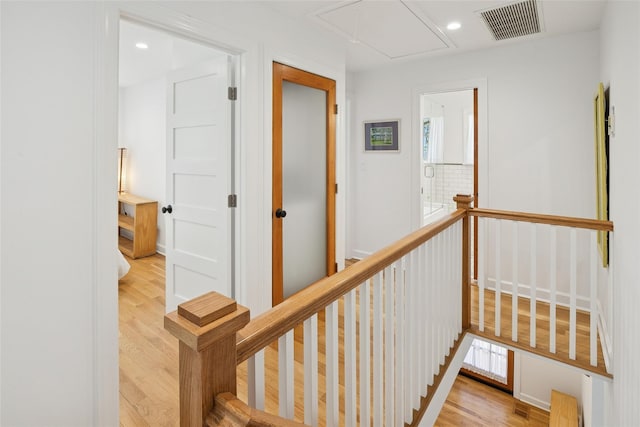hallway with an upstairs landing, attic access, wood finished floors, and visible vents