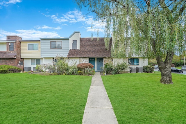 townhome / multi-family property featuring roof with shingles, stone siding, cooling unit, and a front yard