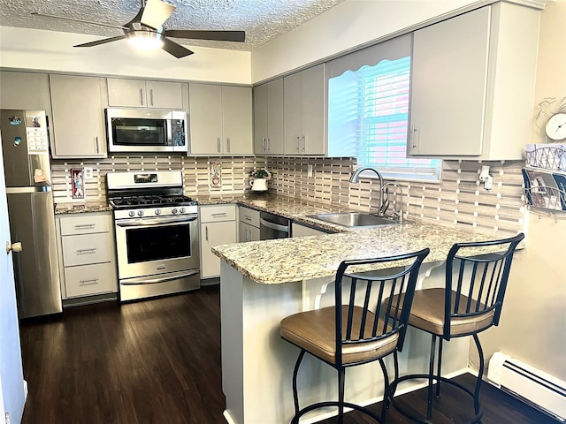 kitchen with a peninsula, a sink, baseboard heating, a ceiling fan, and appliances with stainless steel finishes