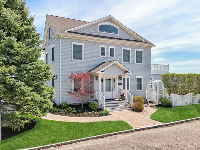 greek revival inspired property with fence, covered porch, a shingled roof, and a front lawn
