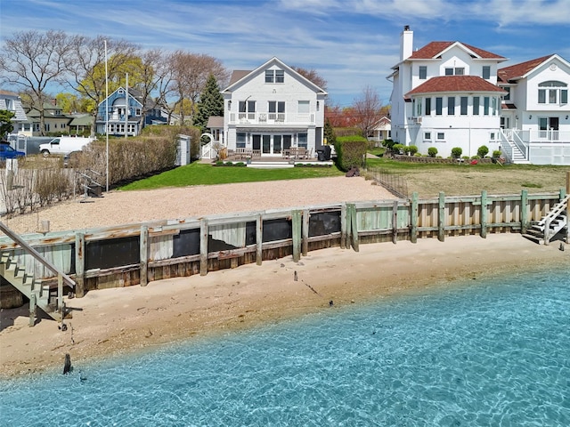rear view of property featuring a water view, fence, stairs, and a view of the beach