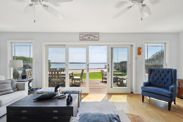 living room featuring a ceiling fan, a healthy amount of sunlight, light wood-style flooring, and a water view