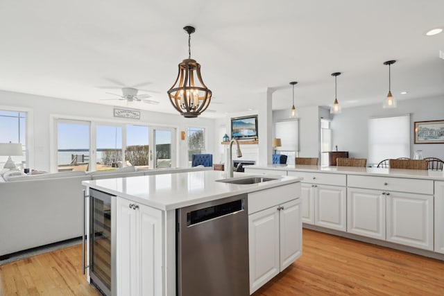 kitchen featuring stainless steel dishwasher, a sink, light countertops, beverage cooler, and open floor plan