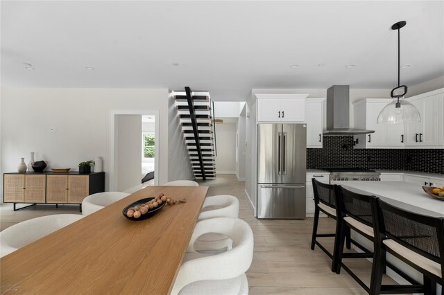 260 Wilmot Rd, Ocean Beach, NY 11770 - kitchen with decorative backsplash, high end fridge, wall chimney exhaust hood, white cabinets, and light wood finished floors