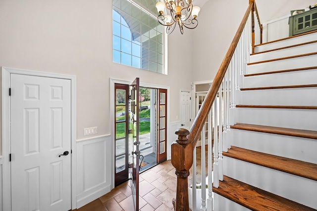 entryway with an inviting chandelier, stairs, a high ceiling, and wainscoting