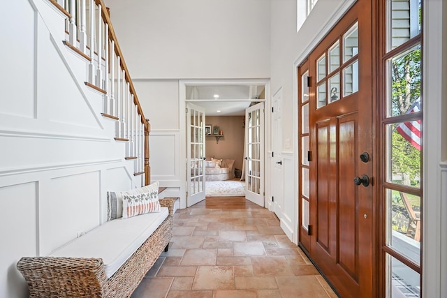 foyer entrance with a high ceiling, a decorative wall, french doors, stairs, and stone tile flooring