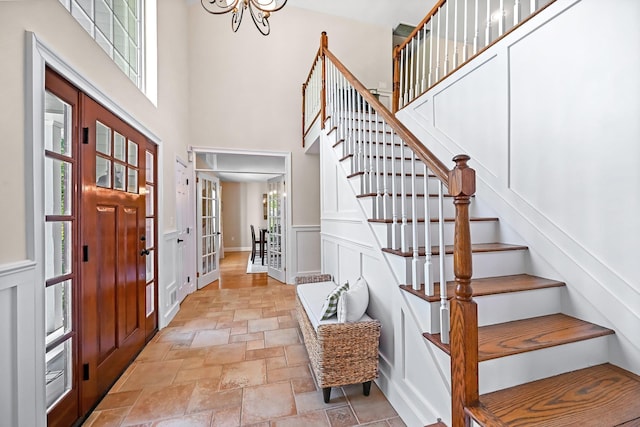 foyer entrance with stone tile flooring, a towering ceiling, baseboards, stairway, and a chandelier