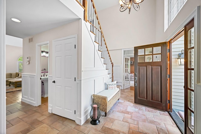 foyer featuring visible vents, stone tile floors, wainscoting, stairway, and a chandelier