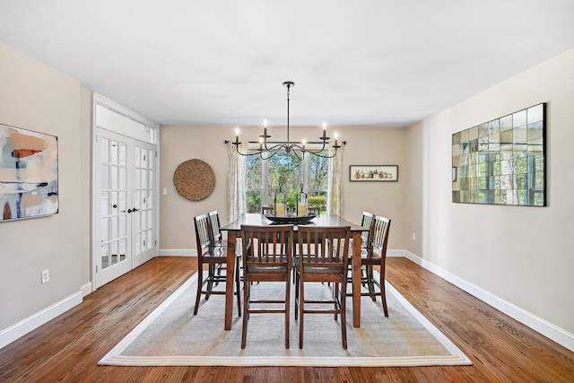 dining space with french doors, baseboards, a notable chandelier, and wood finished floors