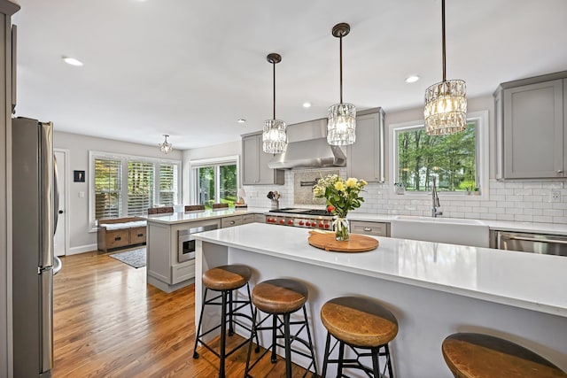 kitchen featuring a peninsula, gray cabinets, wall chimney exhaust hood, a sink, and stainless steel appliances
