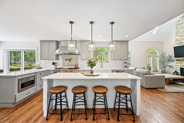 kitchen featuring a kitchen breakfast bar, gray cabinets, wall chimney exhaust hood, stainless steel microwave, and backsplash