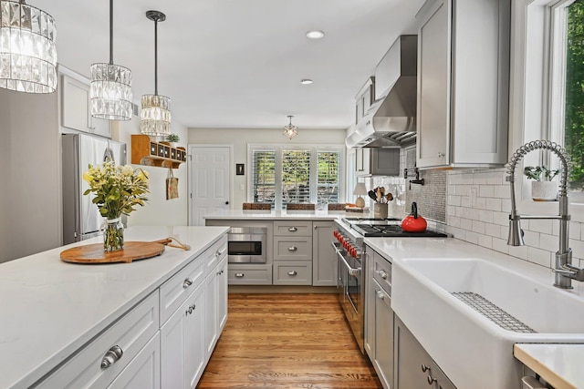 kitchen featuring appliances with stainless steel finishes, a sink, light wood finished floors, wall chimney exhaust hood, and backsplash