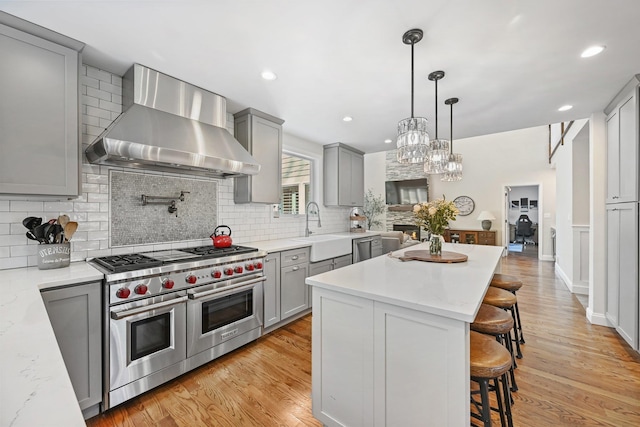 kitchen with wall chimney range hood, appliances with stainless steel finishes, gray cabinetry, and a sink