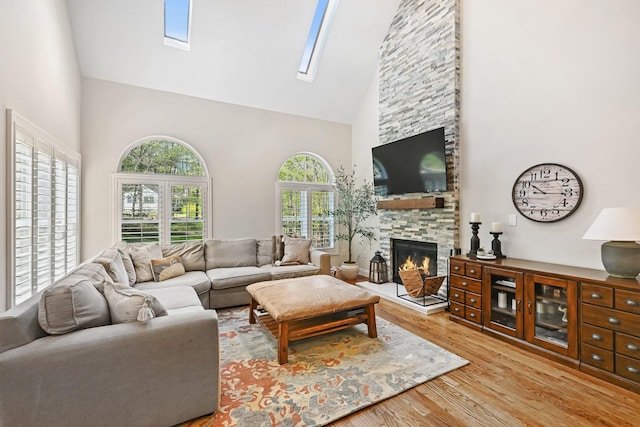living room with light wood-style flooring, a fireplace, a skylight, and high vaulted ceiling
