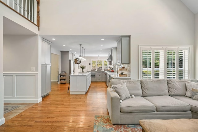 living area featuring wainscoting, a towering ceiling, a decorative wall, light wood-type flooring, and recessed lighting