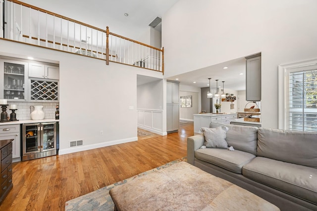 living room featuring light wood-style floors, a towering ceiling, visible vents, a dry bar, and wine cooler