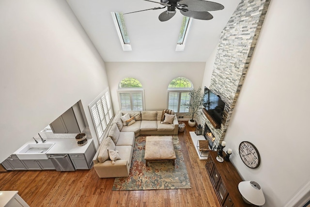living area with high vaulted ceiling, a skylight, ceiling fan, and wood finished floors