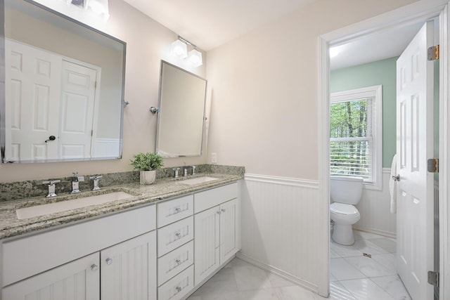 bathroom featuring double vanity, toilet, wainscoting, and a sink