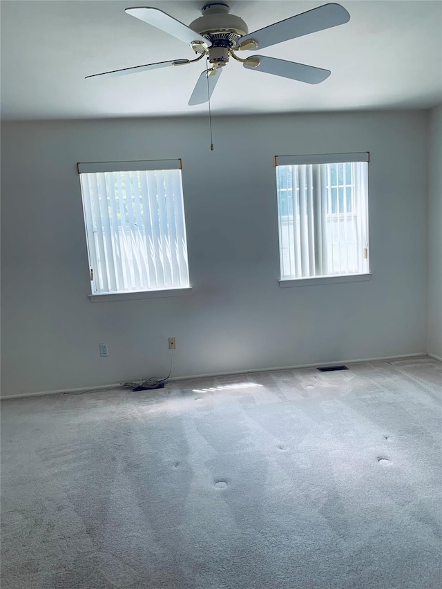 carpeted empty room featuring a ceiling fan, visible vents, and baseboards