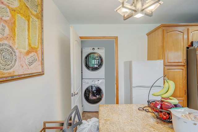 laundry room with tile patterned floors, stacked washer and clothes dryer, a notable chandelier, and laundry area