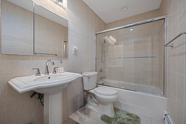 bathroom featuring tile patterned floors, a baseboard heating unit, tile walls, toilet, and bath / shower combo with glass door