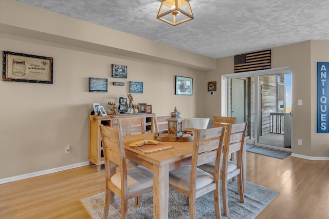 dining space with a textured ceiling, baseboards, and light wood-style flooring