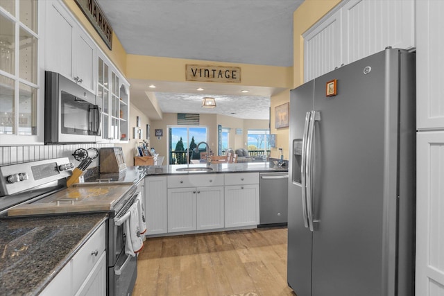 kitchen featuring a sink, a peninsula, light wood finished floors, glass insert cabinets, and stainless steel appliances