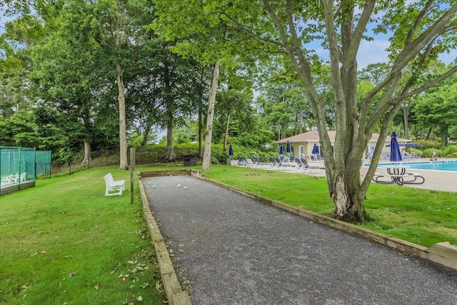 view of community with aphalt driveway, fence, a yard, and a pool