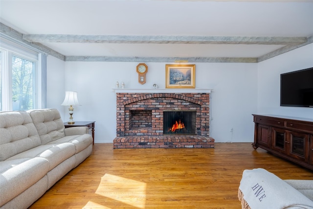 living room featuring a brick fireplace, beam ceiling, wood finished floors, and baseboards