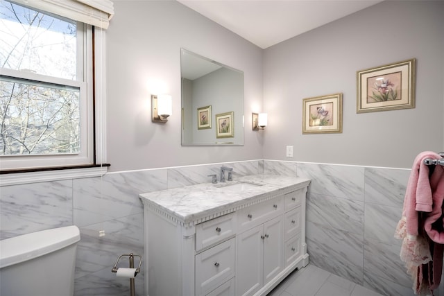 bathroom featuring toilet, tile walls, wainscoting, and vanity