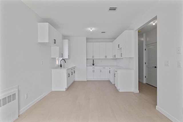 kitchen with radiator heating unit, light wood finished floors, a sink, and visible vents