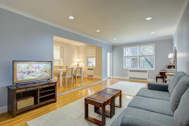 living area with radiator heating unit, baseboards, light wood-style floors, and ornamental molding